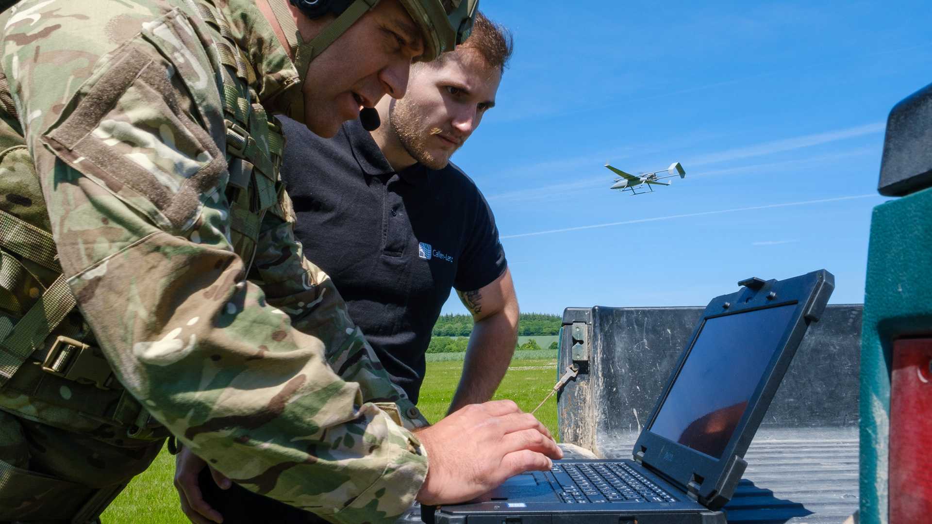 Military personnel using a laptop and a drone in the background